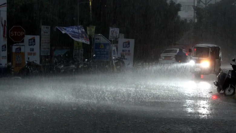 Heavy monsoon rain causing waterlogging on a busy city street in Raipur Chhattisgarh with vehicles driving through water.