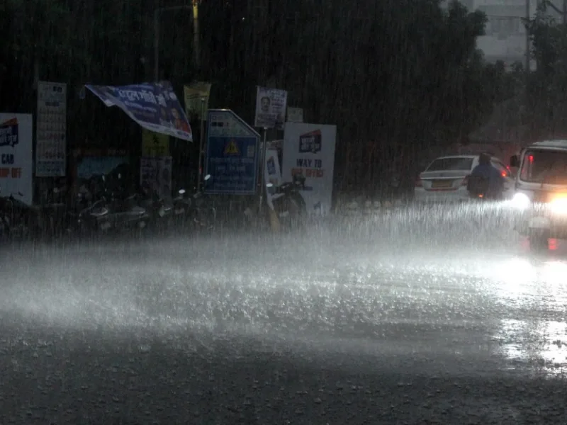 Heavy monsoon rain causing waterlogging on a busy city street in Raipur Chhattisgarh with vehicles driving through water.