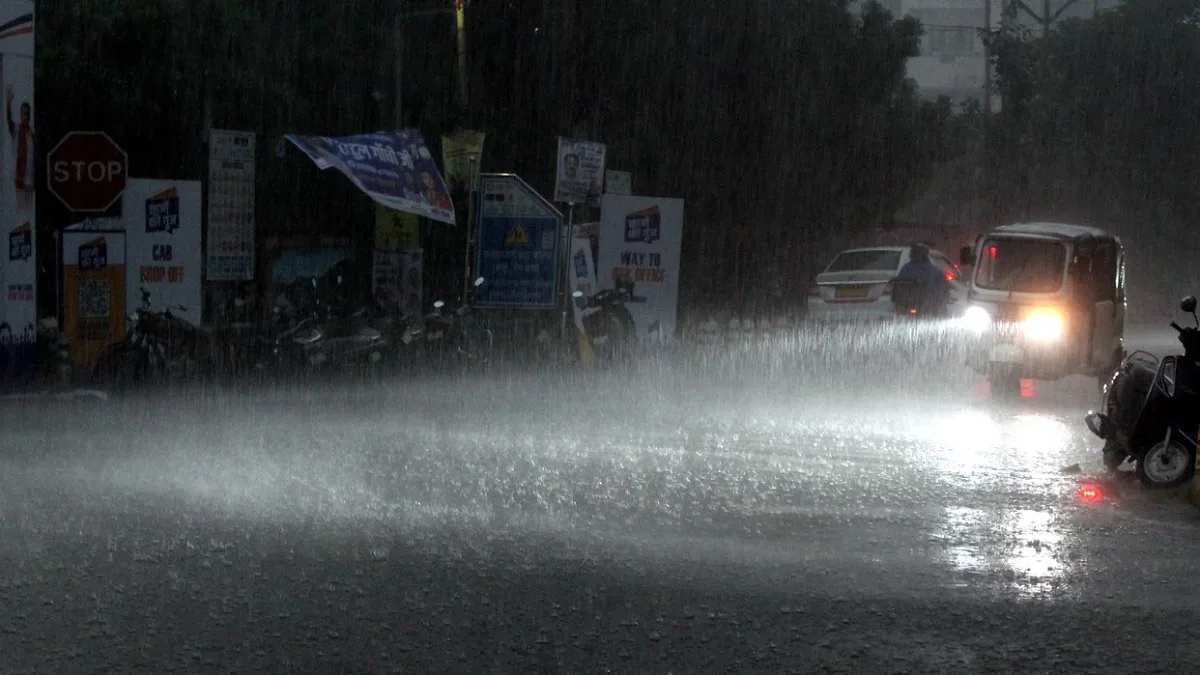 Heavy monsoon rain causing waterlogging on a busy city street in Raipur Chhattisgarh with vehicles driving through water.