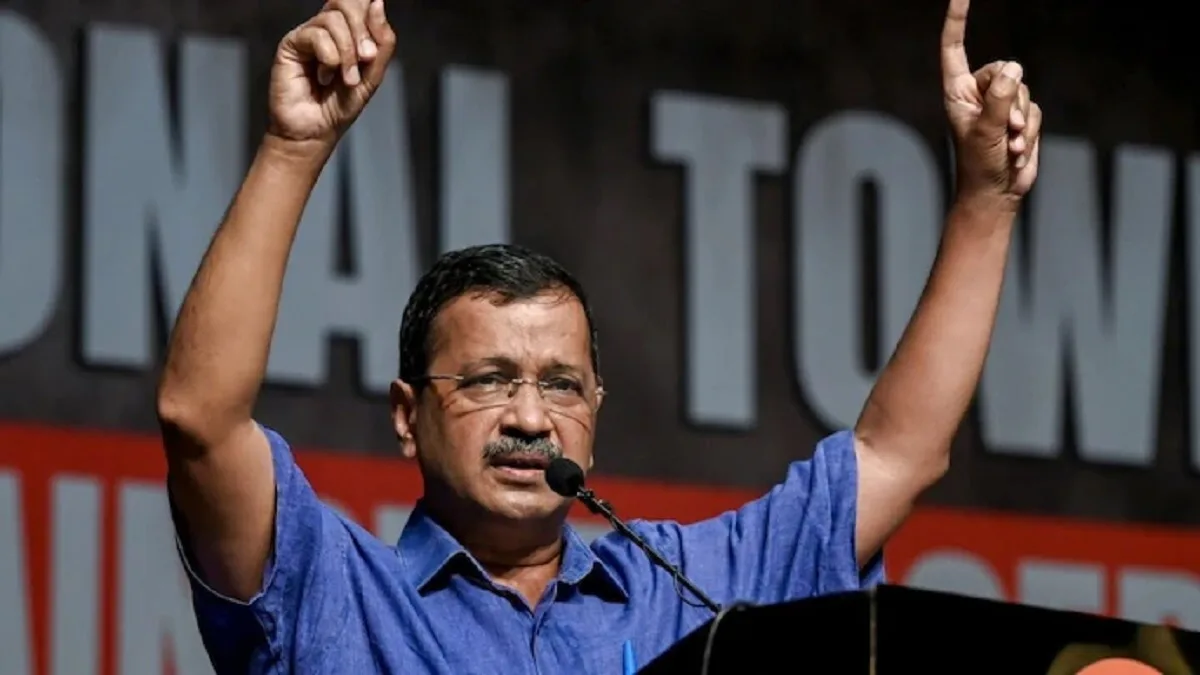 मंच से भाषण देते हुए अरविंद केजरीवाल, दोनों हाथ ऊपर उठाकर लोगों को संबोधित करते हुए।